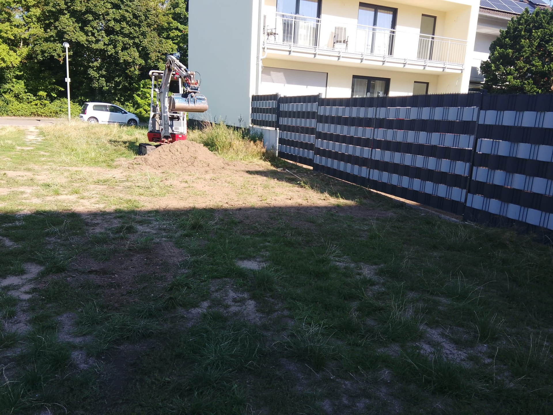 Minibagger beim Aushub neben einem Erdhügel an einer Baustelle