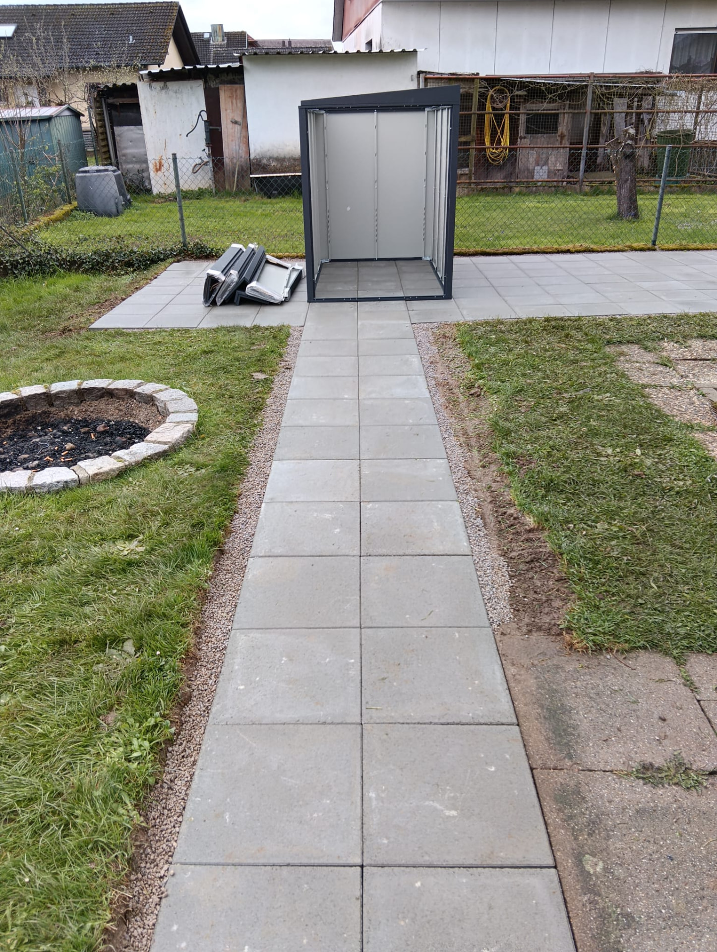 Verlegter Terrassen- und Wegebau aus Steinplatten mit Gartenhaus und Beet